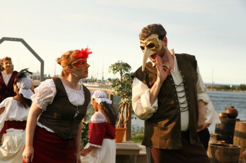 Actors in masquerade masks on outdoor stage at Collingwood waterfront for Theatre Georgian Bay